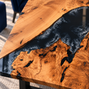Close-up of poplar wood grain meeting glossy black epoxy resin with smoky gray swirls along an irregular wood edge.